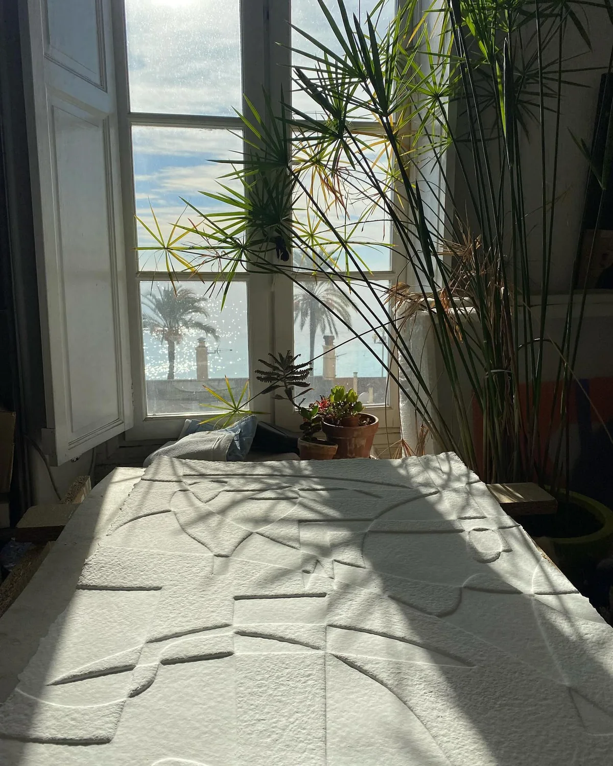 Le soleil de Nice traverse la fenêtre de l'atelier et rase un grand relief blanc